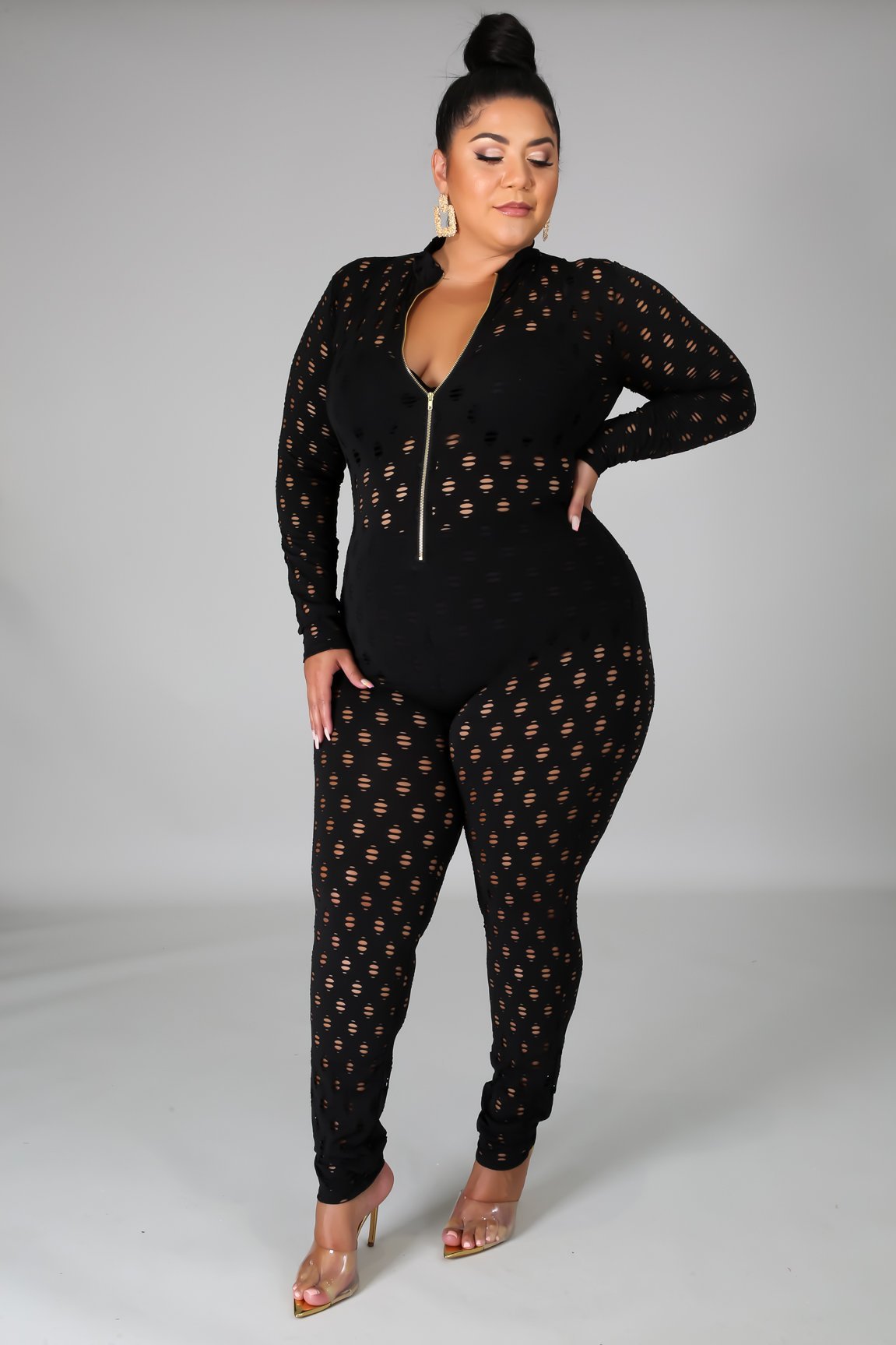 Curvy women zip front jumpsuit in black with long sleeves and cutout details worn with clear heels