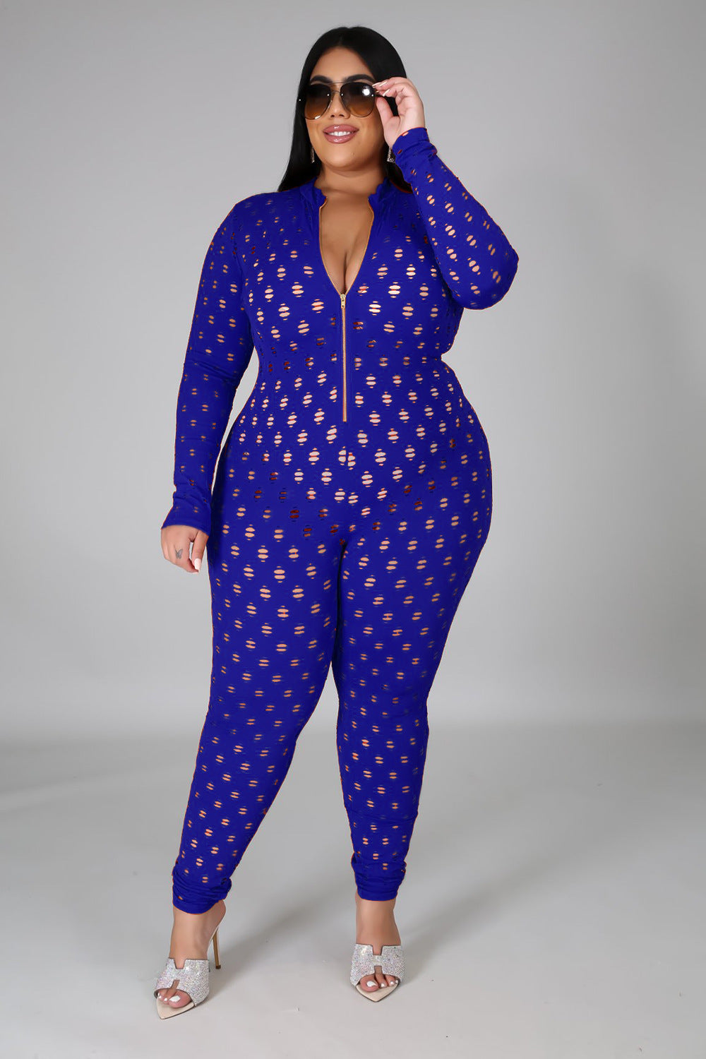 Curvy women zip front jumpsuit in blue with long sleeves and cutout pattern worn with heels and sunglasses